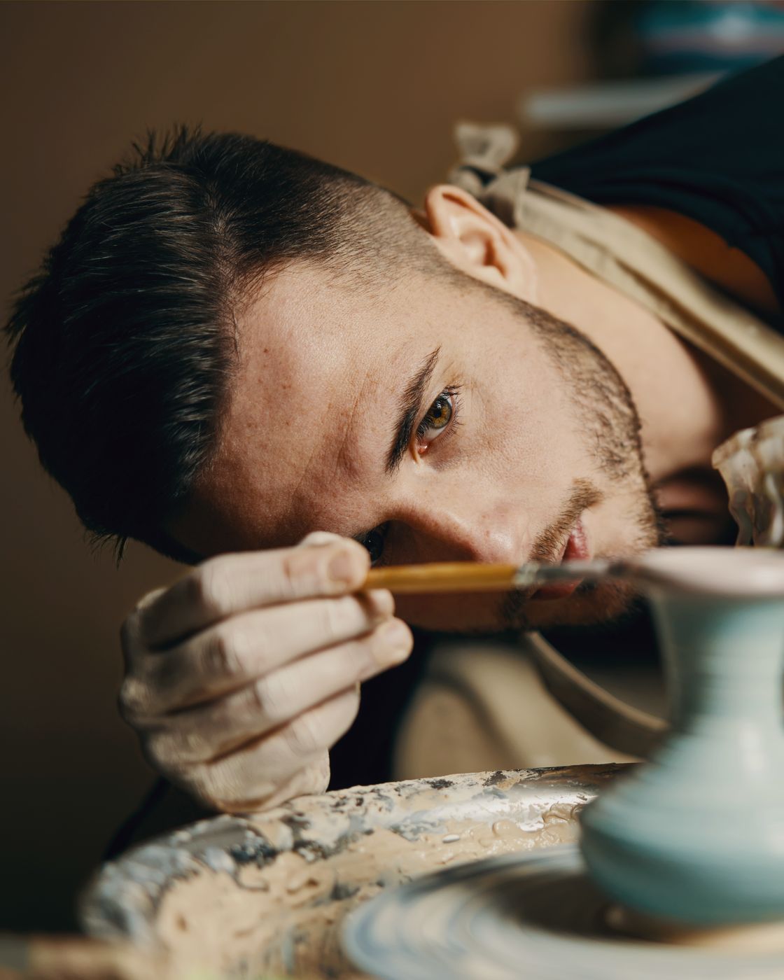 A young man shaping a vase on a pottery wheel, absorbed in the work