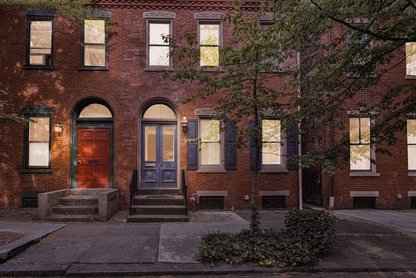 Nineteenth-century brick rowhouses at dusk, a red door and a blue door lit by porch lanterns